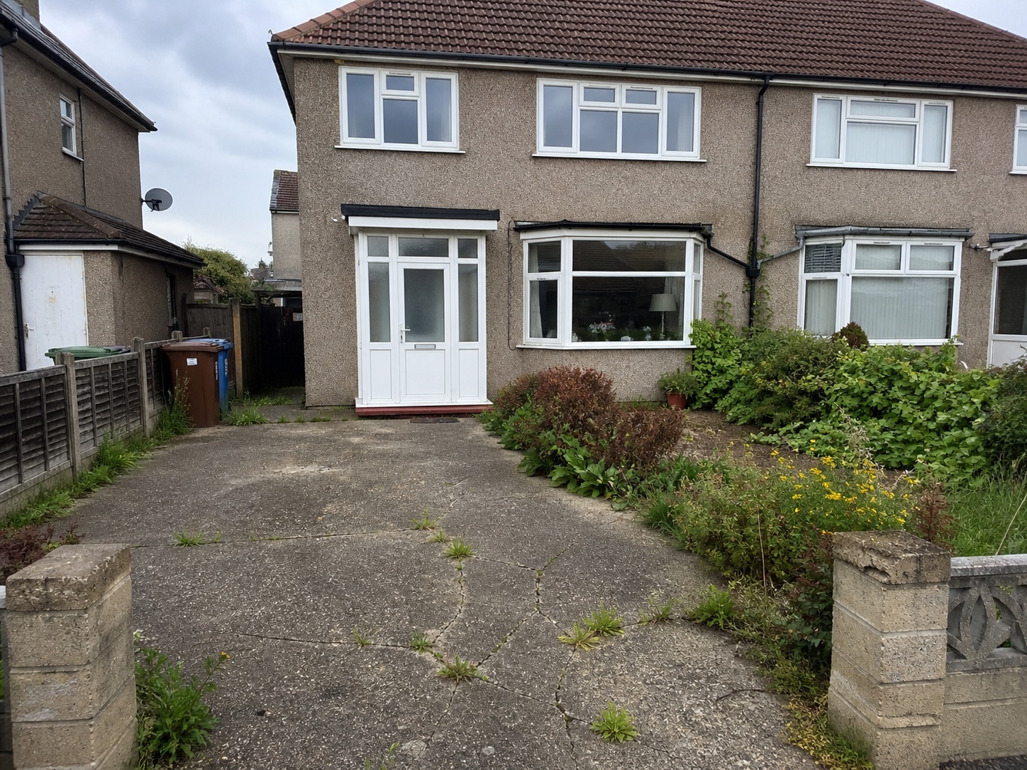 Overgrown front garden and cracked driveway at a UK house, used as a before image in an AI mock-up