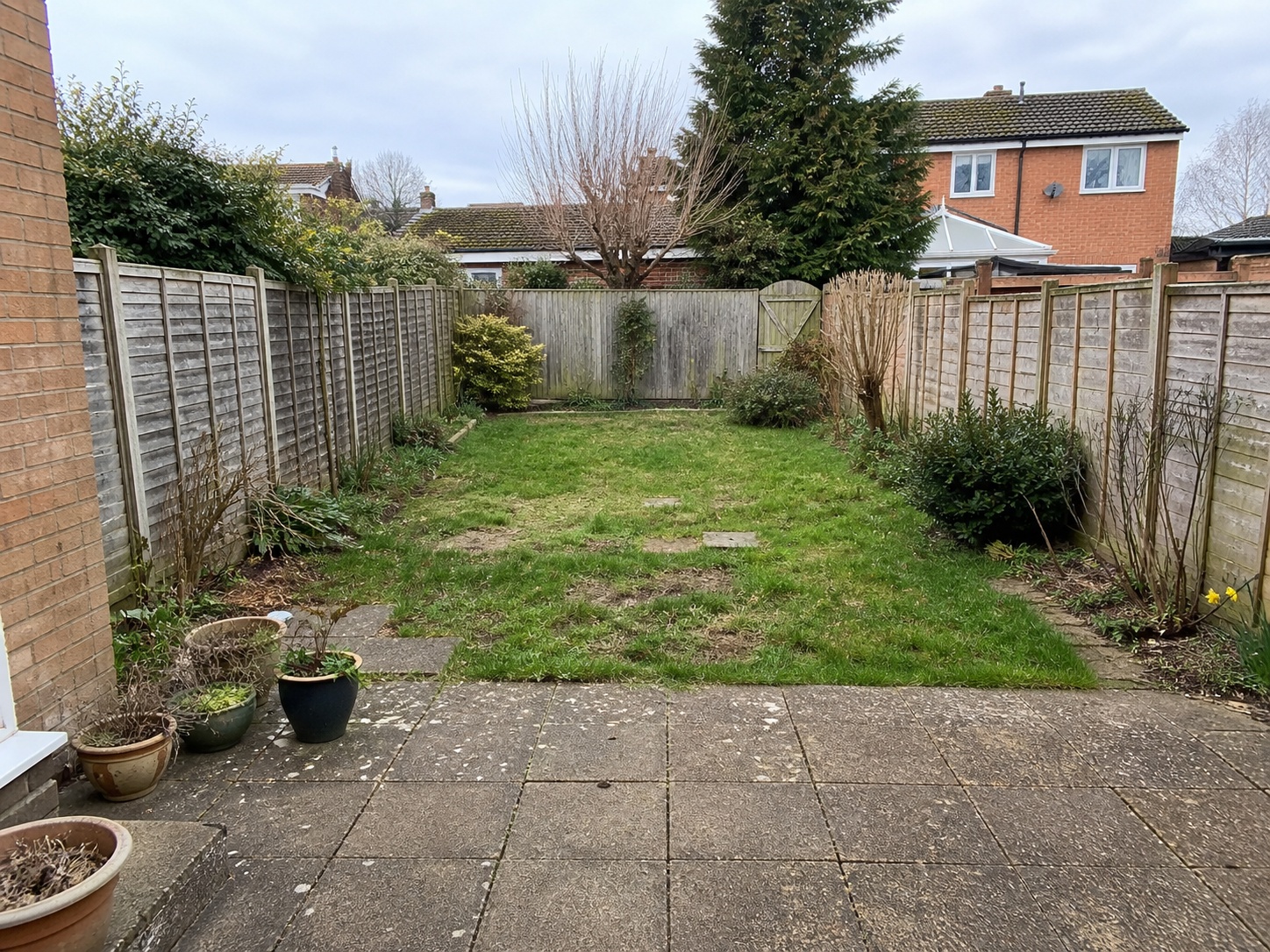 Tired rear garden with worn paving and patchy grass, before image of an AI landscaping mock-up